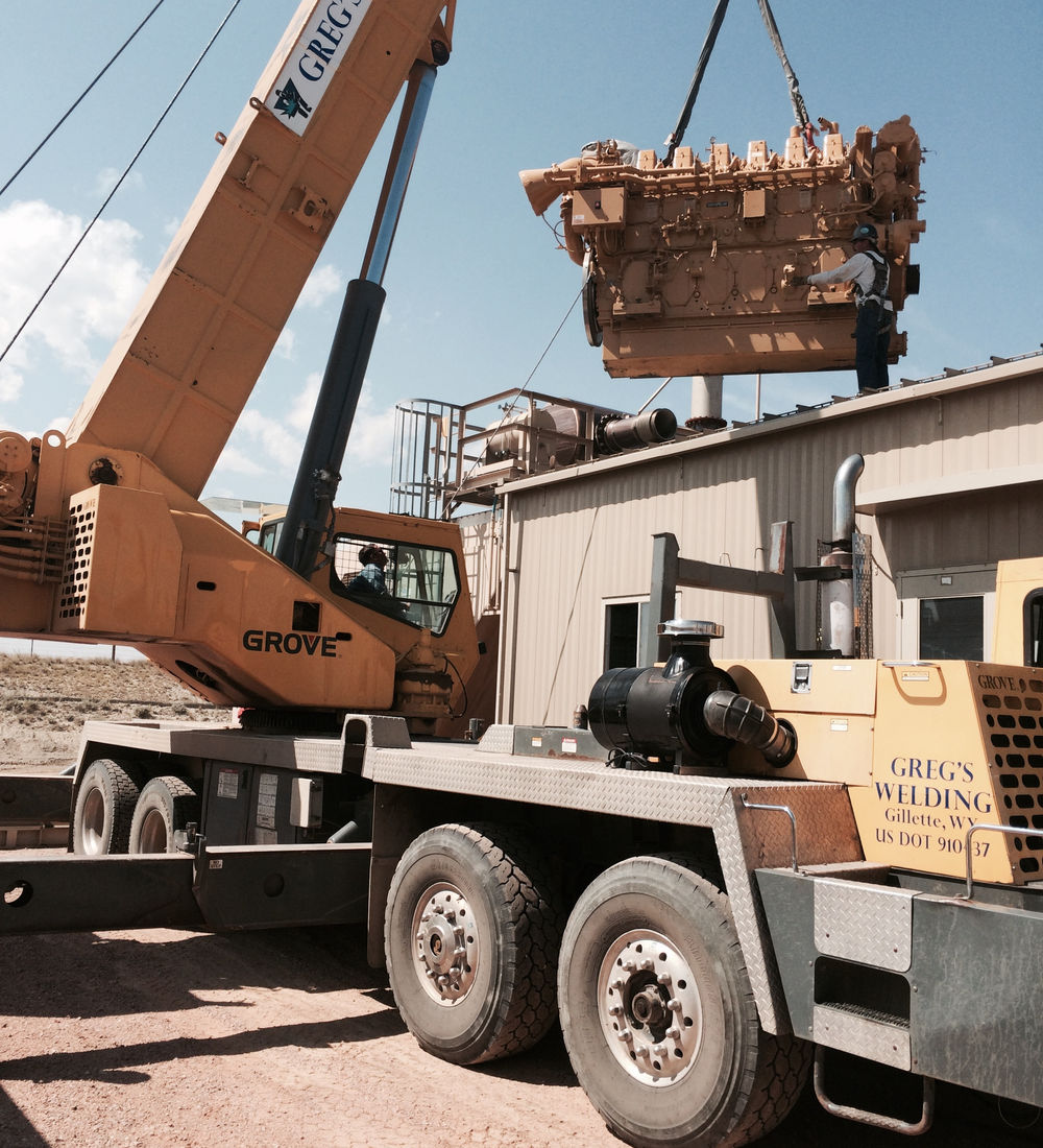 A truck-mounted crane lifting a large engine onto a trailer